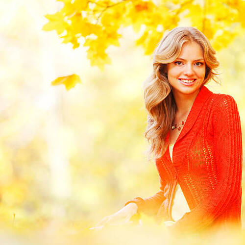 Happy young woman sitting on autumn leaves in park.jpg