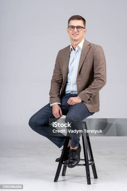 handsome businessman isolated on light gray background young male in suit is sitting on chair.jpg