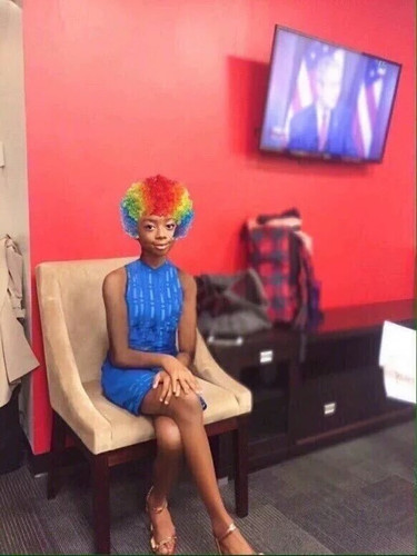 clown shit 03 thin black girl sitting w her legs crossed wearing a multicolored clown wig.jpg