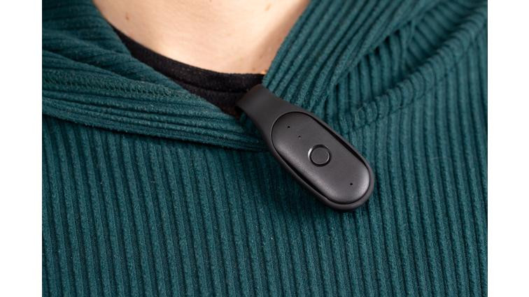 None Bee AI pin clipped to a person’s collar, on top of a green, ribbed sweater.