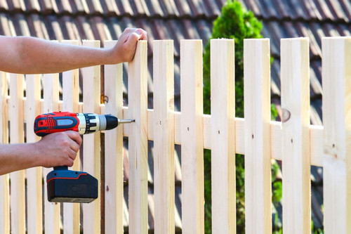 building a wooden fence with a drill and screw. Close up of his hand and the tool in a DIY concept..jpg