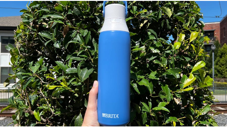 None A hand holding Brita Stainless Steel Filtering Water Bottle in front of a tree.