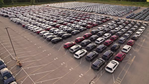 Aerial view of car storage or parking lot new unsold EV cars. Vehicle automaker and manufacturer par.jpg