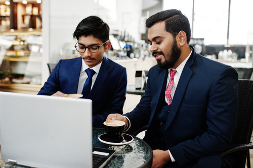 Two indian business man in suits sitting at office on cafe, looking at laptop and drinking coffee..jpg