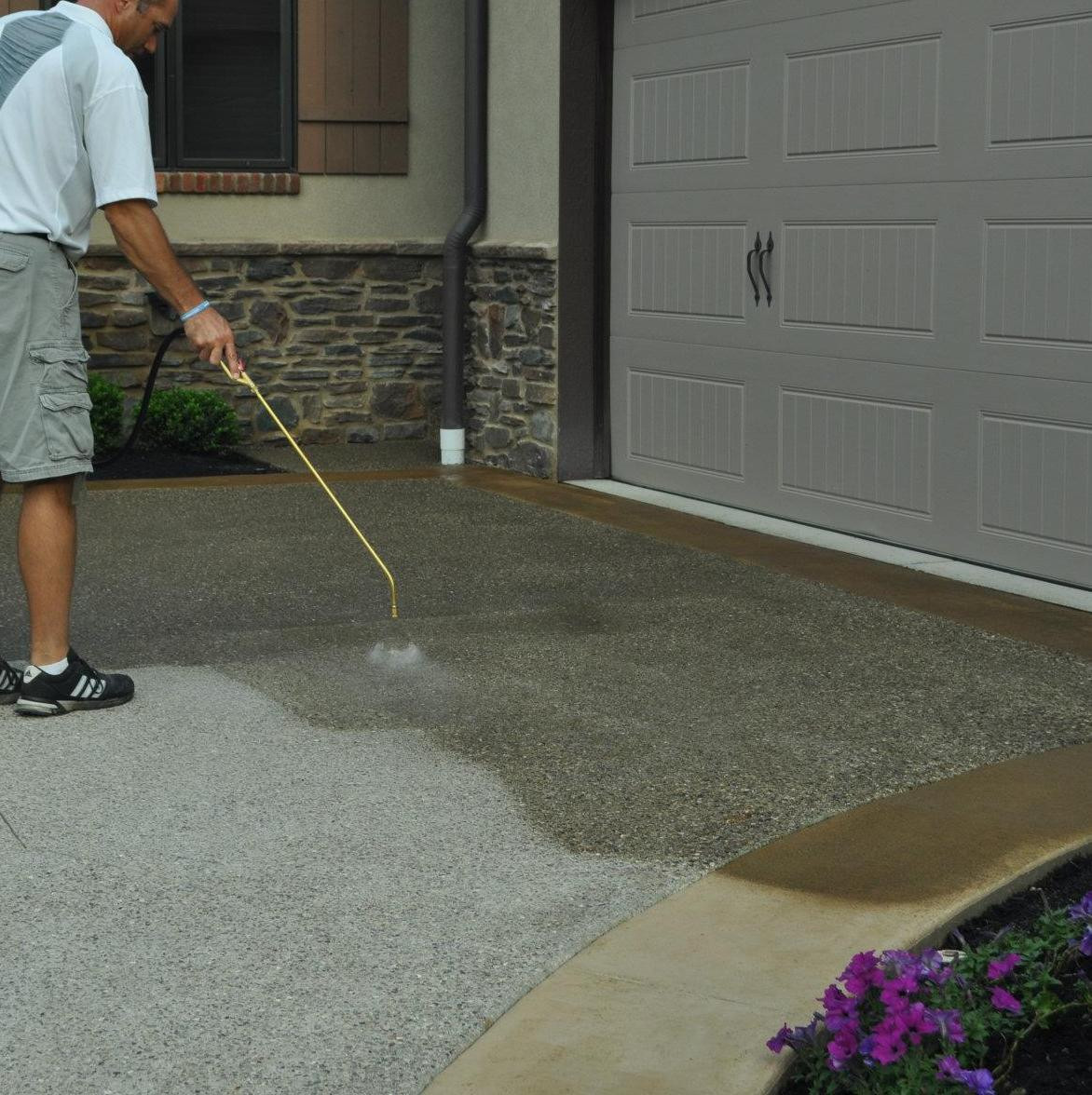 Professional spraying concrete sealer on a residential driveway showing wet sealed finish