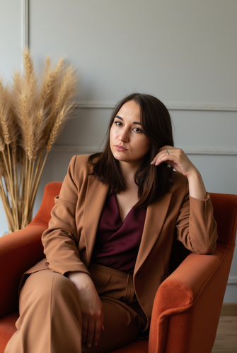 a light skinned woman in her 30s is seated in a mid century modern burnt orange velvet armchair she .png
