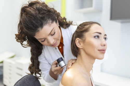Dermatologist in latex gloves holding dermatoscope while examining attractive patient with skin dise.jpg