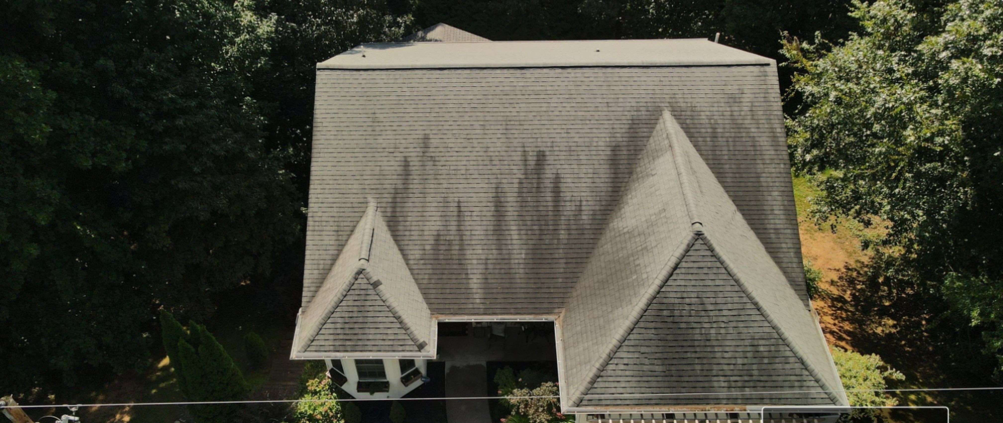 Aerial drone view of roof covered in dark black algae streaks before soft wash cleaning