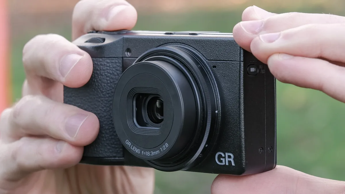 Ricoh GR IV compact camera held in a pair of hands