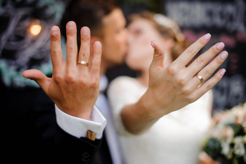 Blurred figures of happy and smiling bridegroom and bride kissing and showing wedding rings on their.jpg