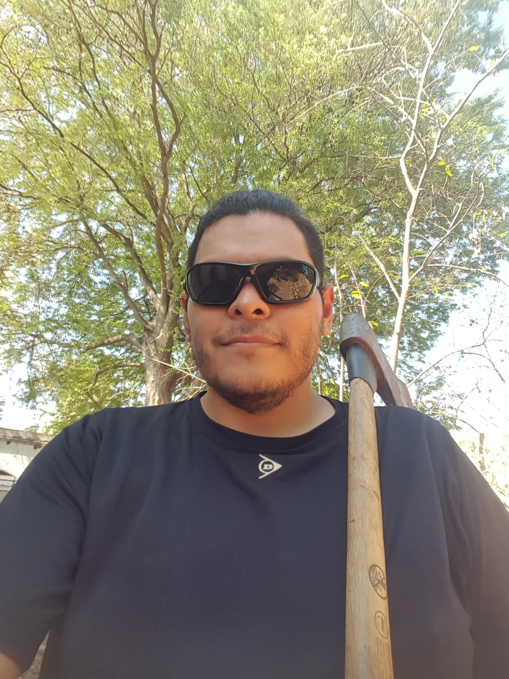 Selfie de Daniel en el jardín con lentes oscuros y un hacha al hombro