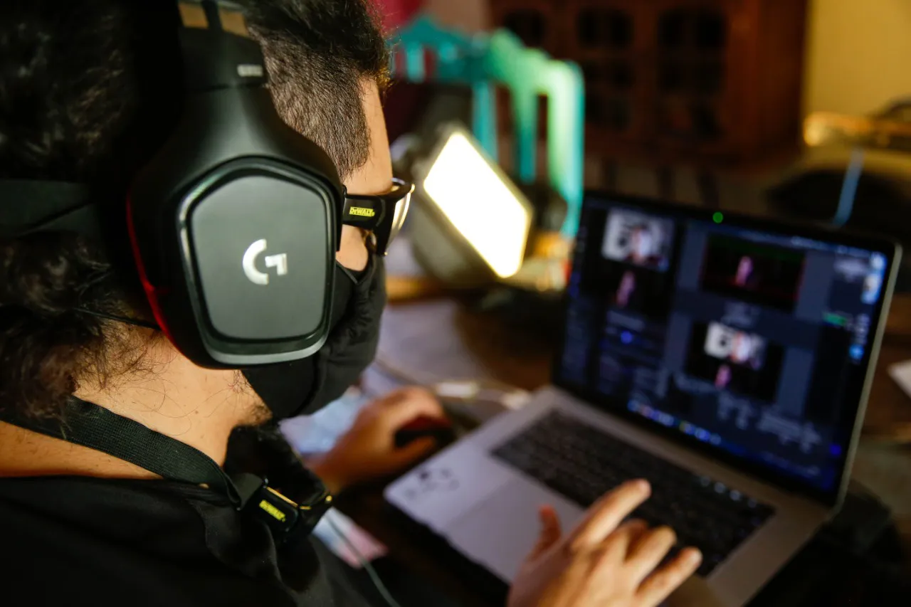 Daniel con lentes, tapabocas y audífonos realizando la transmisión de una entrevista desde la laptop