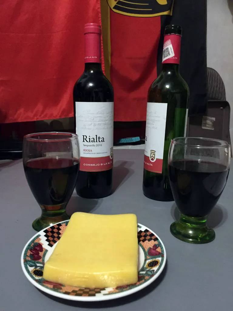 Mesa con dos copas y botellas de vino, y un plato con queso amarillo