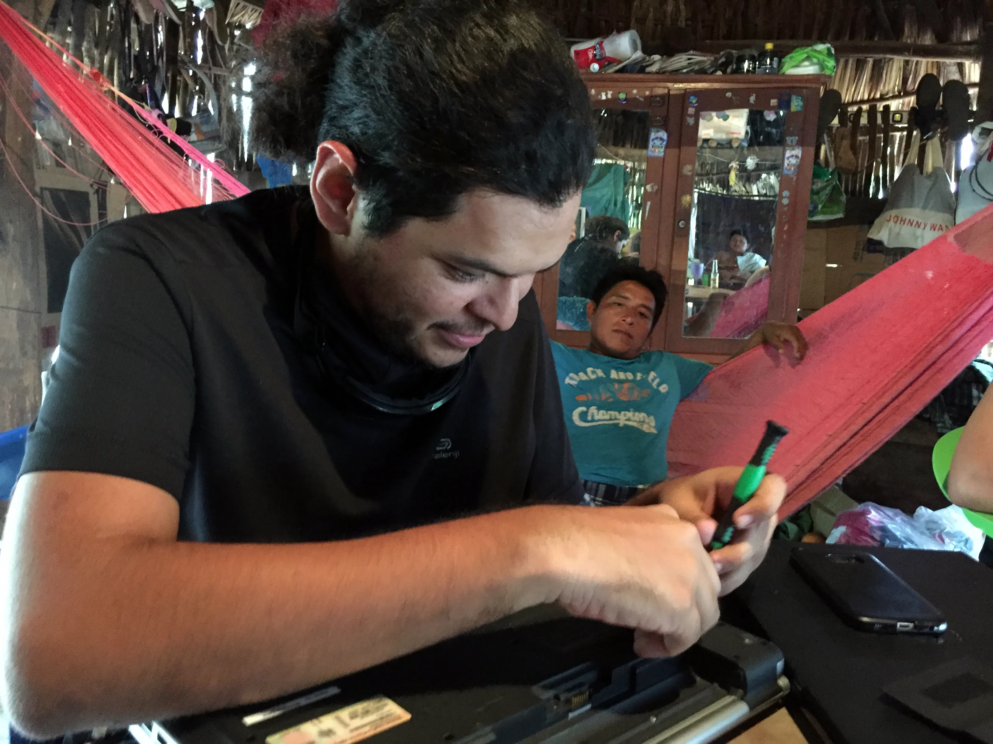 Daniel desatornillando la parte trasera de una laptop mientras una persona mira desde la hamaca
