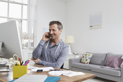 Mann mit Telefon am Schreibtisch in Wohnung, Mnchen, Bayern, Deutschland.jpg