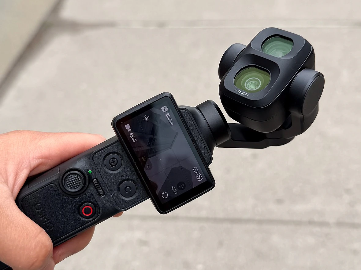 a hand holds a dji gimbal camera over a sidewalk