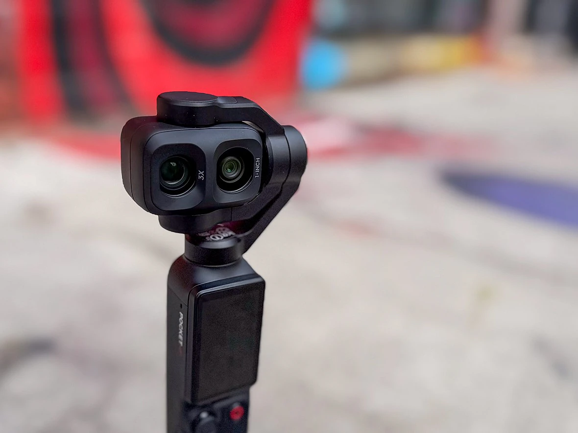 a dji gimabal camera sits on a sidewalk with red graffiti behind it