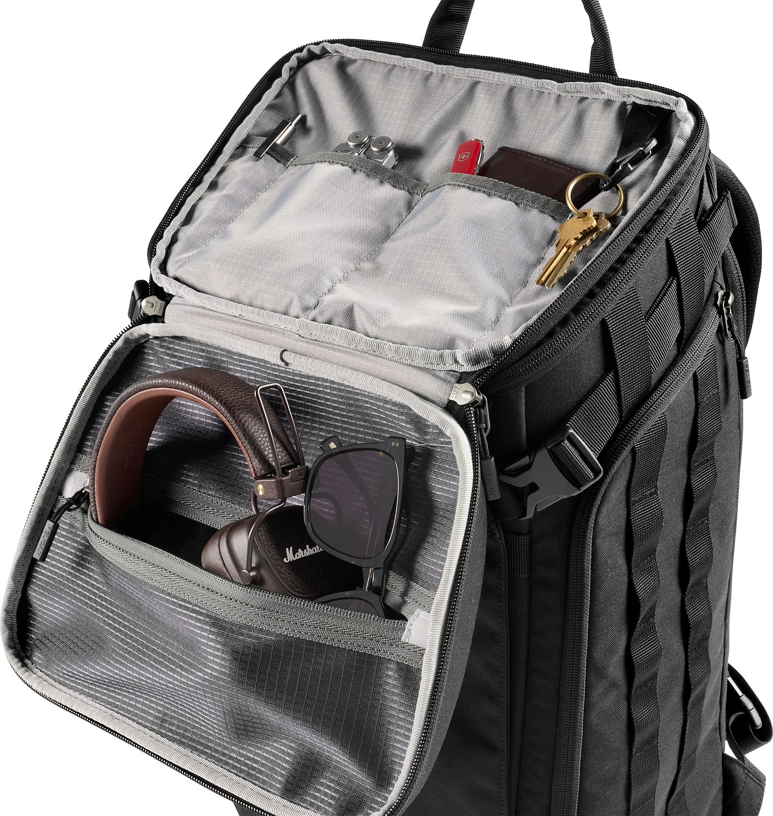A black backpack with its front compartment open, revealing internal pockets containing a multi-tool, a pocket knife, a wallet, keys, headphones, and sunglasses.