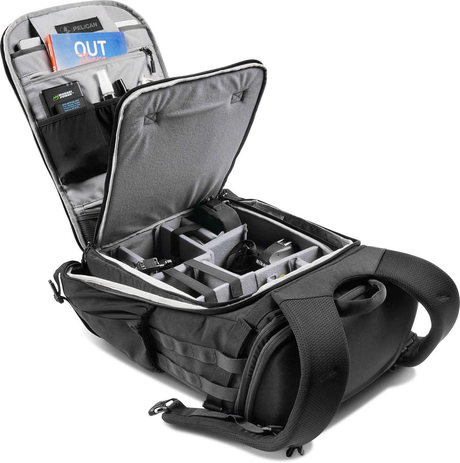 An open black camera backpack lies on its back, revealing interior padded dividers, accessory pockets, and a book labeled "OUT".