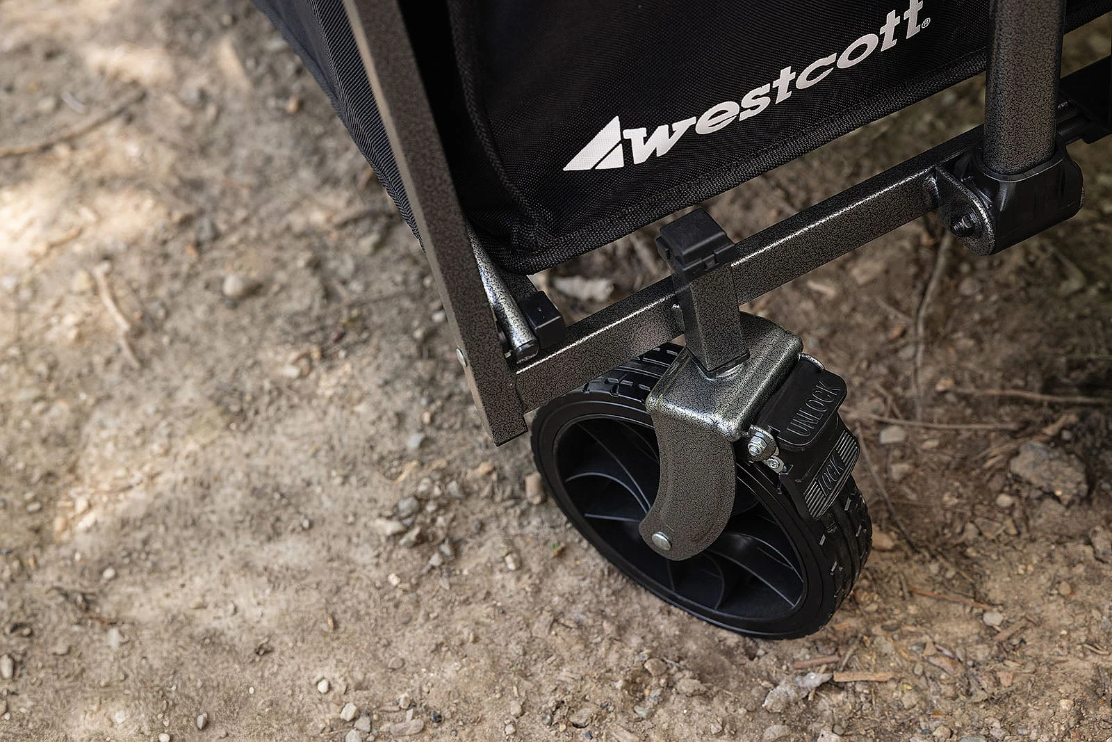 A close-up view of a black Westcott wagon wheel on a dirt path, featuring a locking mechanism on the caster.