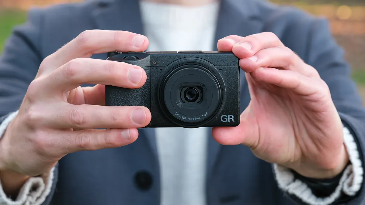 Ricoh GR IV compact camera held in a pair of hands