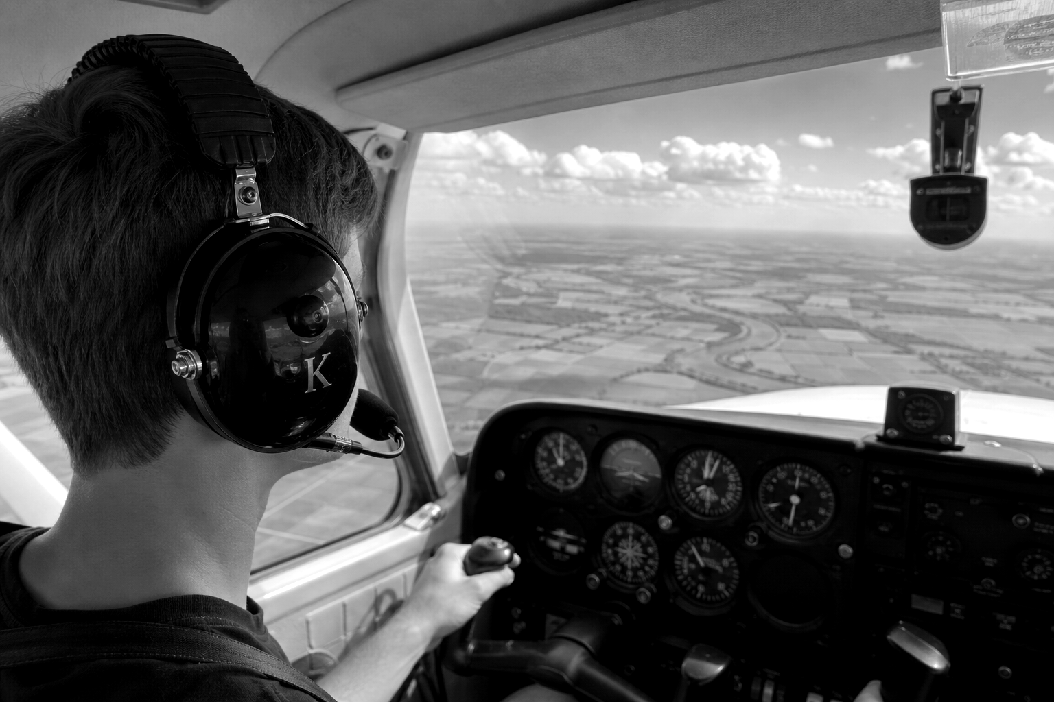 Student pilot wearing aviation headset in Cessna 172 cockpit during a cross country flight over farmland