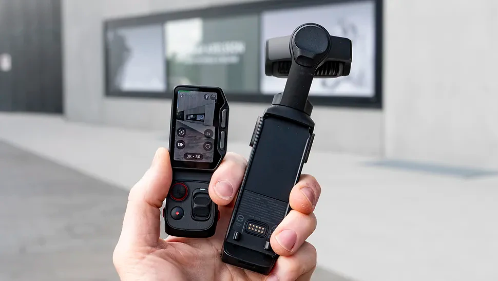 Hand holding the Insta360 Luna Ultra vlogging camera and its screen, outdoors in a grey urban scene