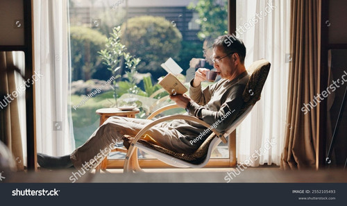 stock photo asian man tea and relax with book on chair for reading story or novel by window at home .jpg
