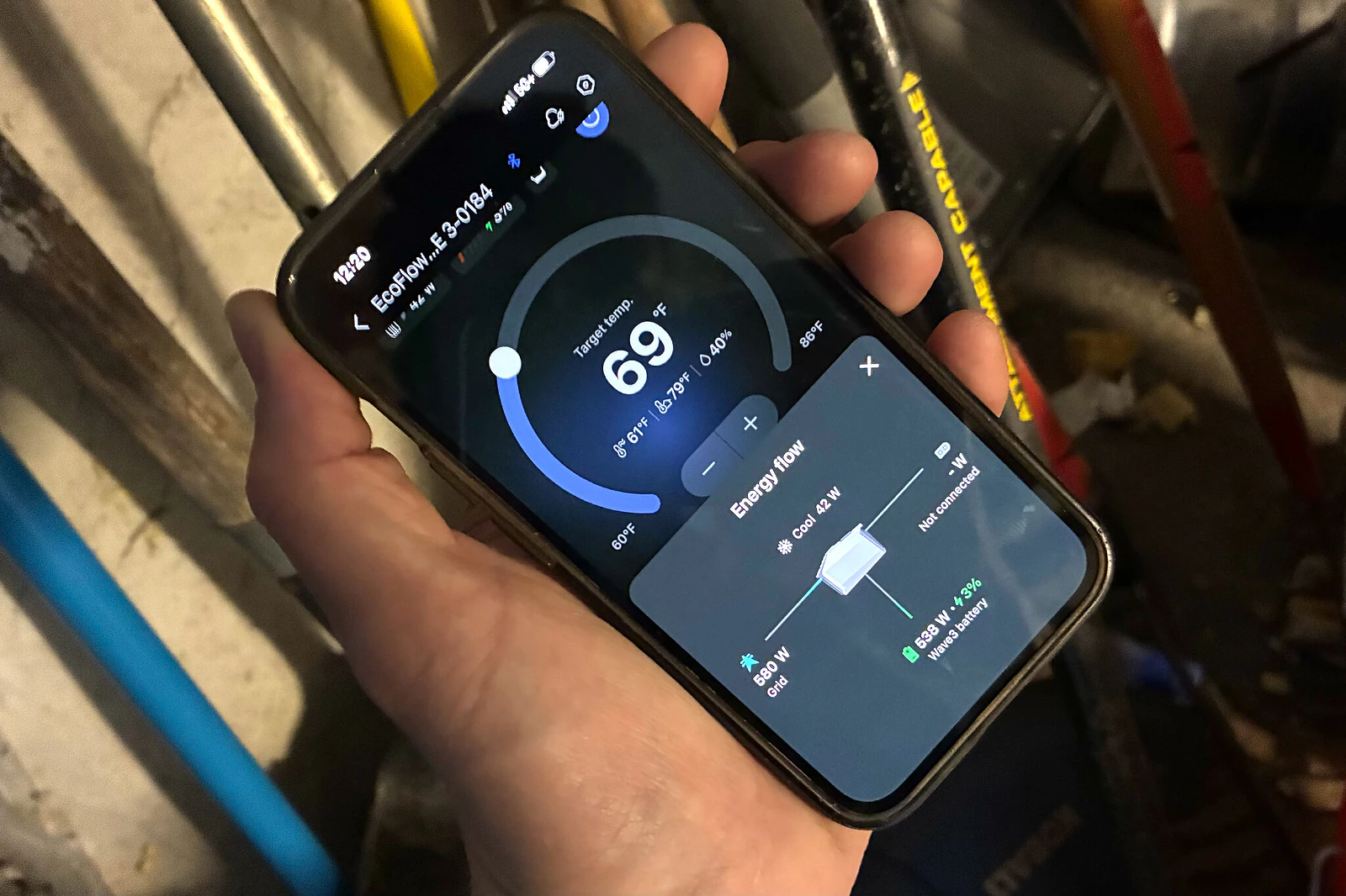 A person's hand holding a smartphone displaying the EcoFlow portable AC app, displaying a digital thermostat and a graphic showing the energy flow around the AC.