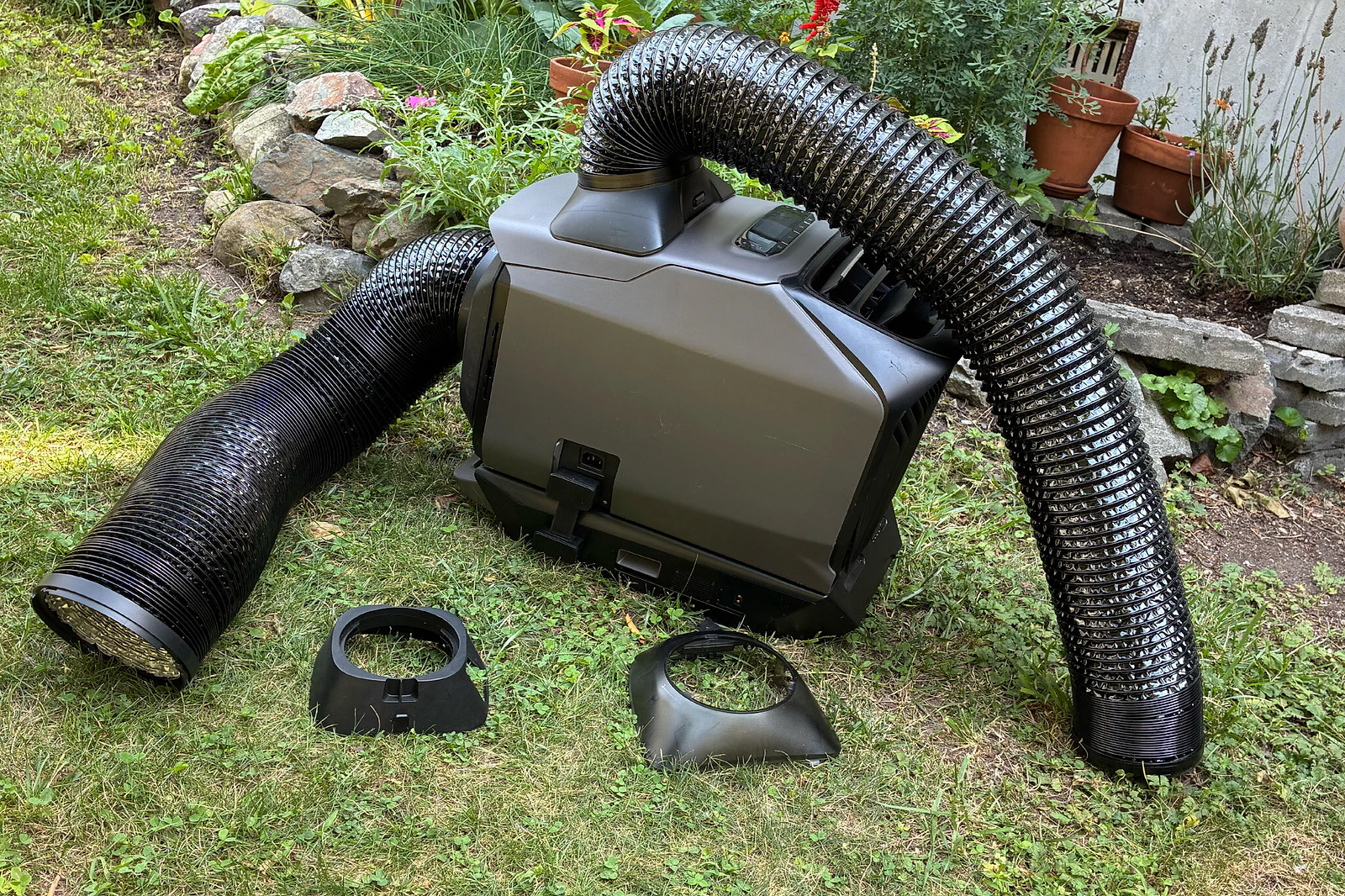 An ultra-portable air conditioner, shown on a grassy lawn with large air-exhaust hoses attached to it in two different places.