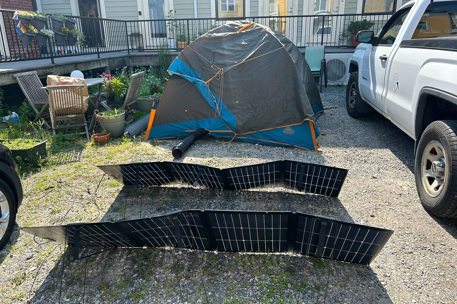 A tent, set up in a driveway, with a black AC air exhaust hose coming out of it.