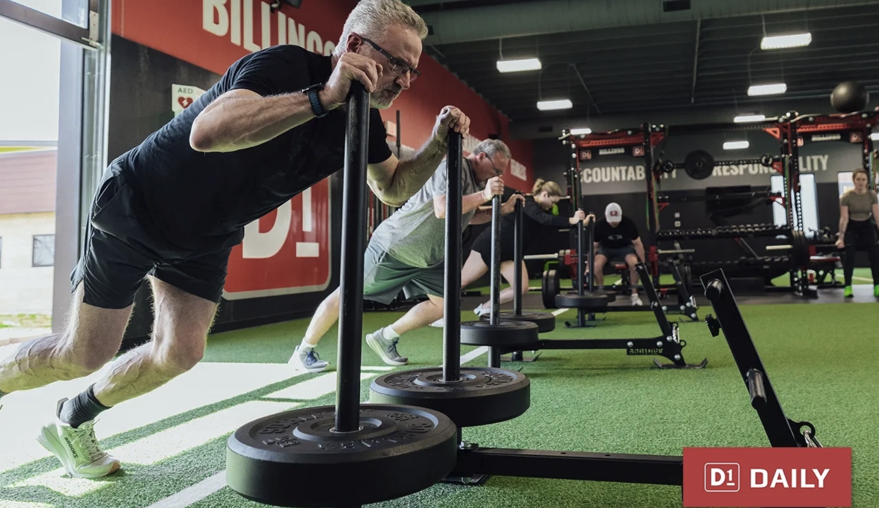 Athletes driving loaded sleds across the turf during a D1 Training conditioning session