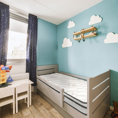 a child's room with blue walls and white furniture, including a small cribe bed in the corner.jpg