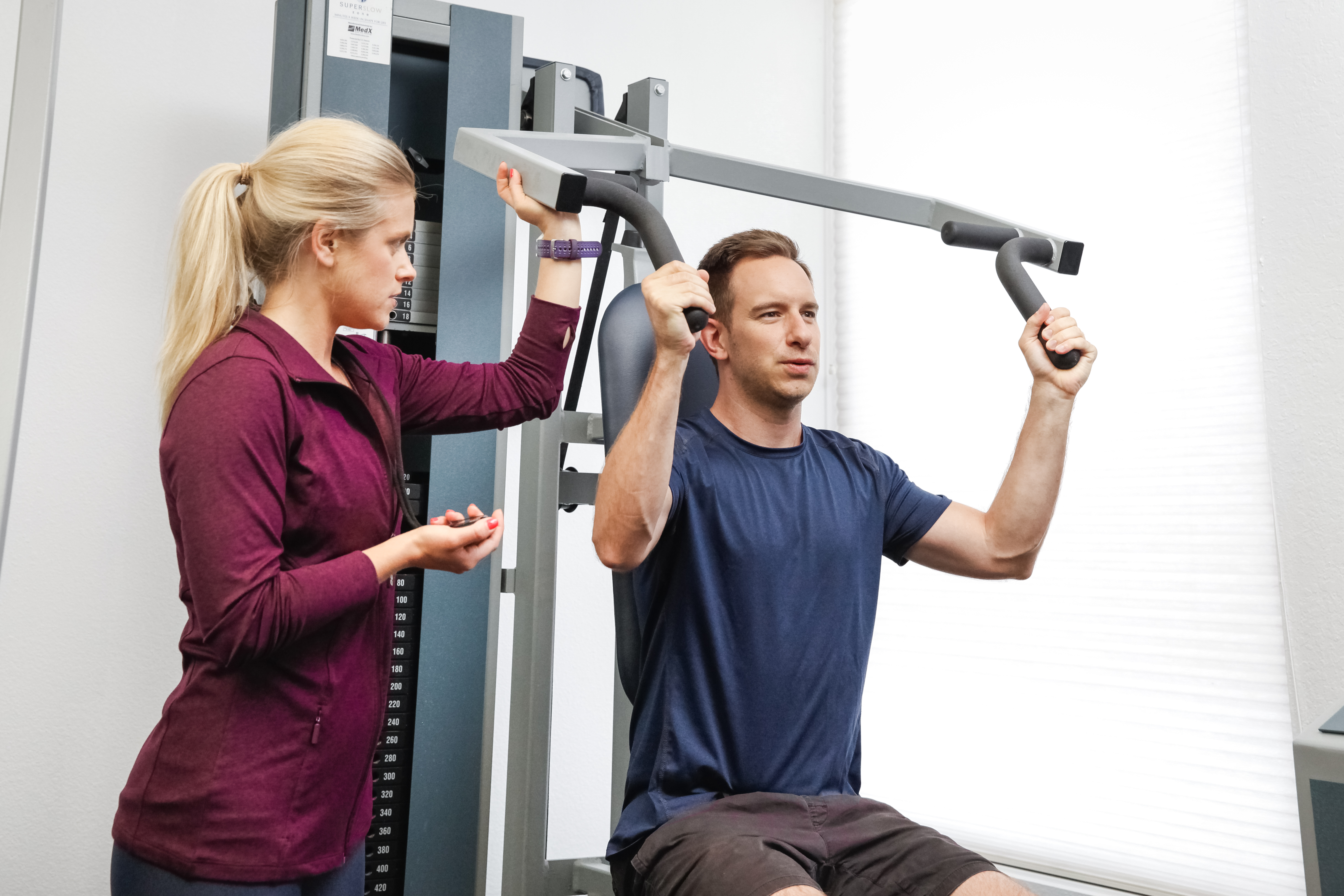 Strength Code trainer supervising a client through an overhead press on a MedX station
