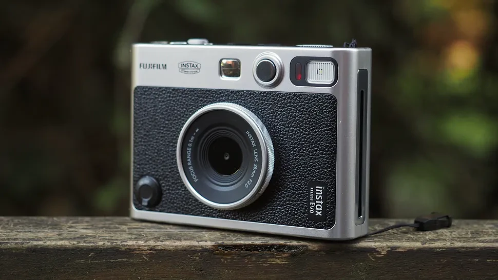 An Instax Mini Evo camera, on a wooden surface in a woodland setting