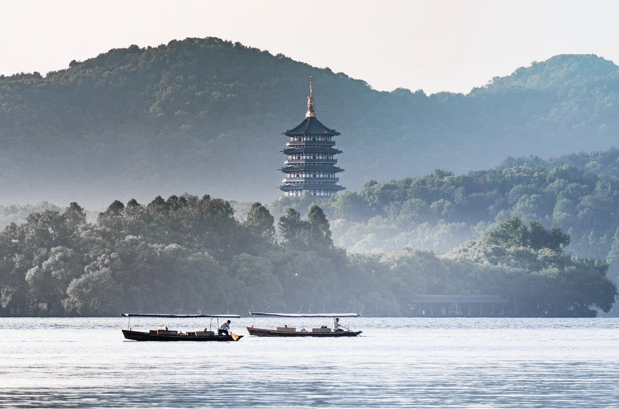 Hangzhou West Lake at dawn with two traditional wooden boats and Leifeng Pagoda in soft misty distance