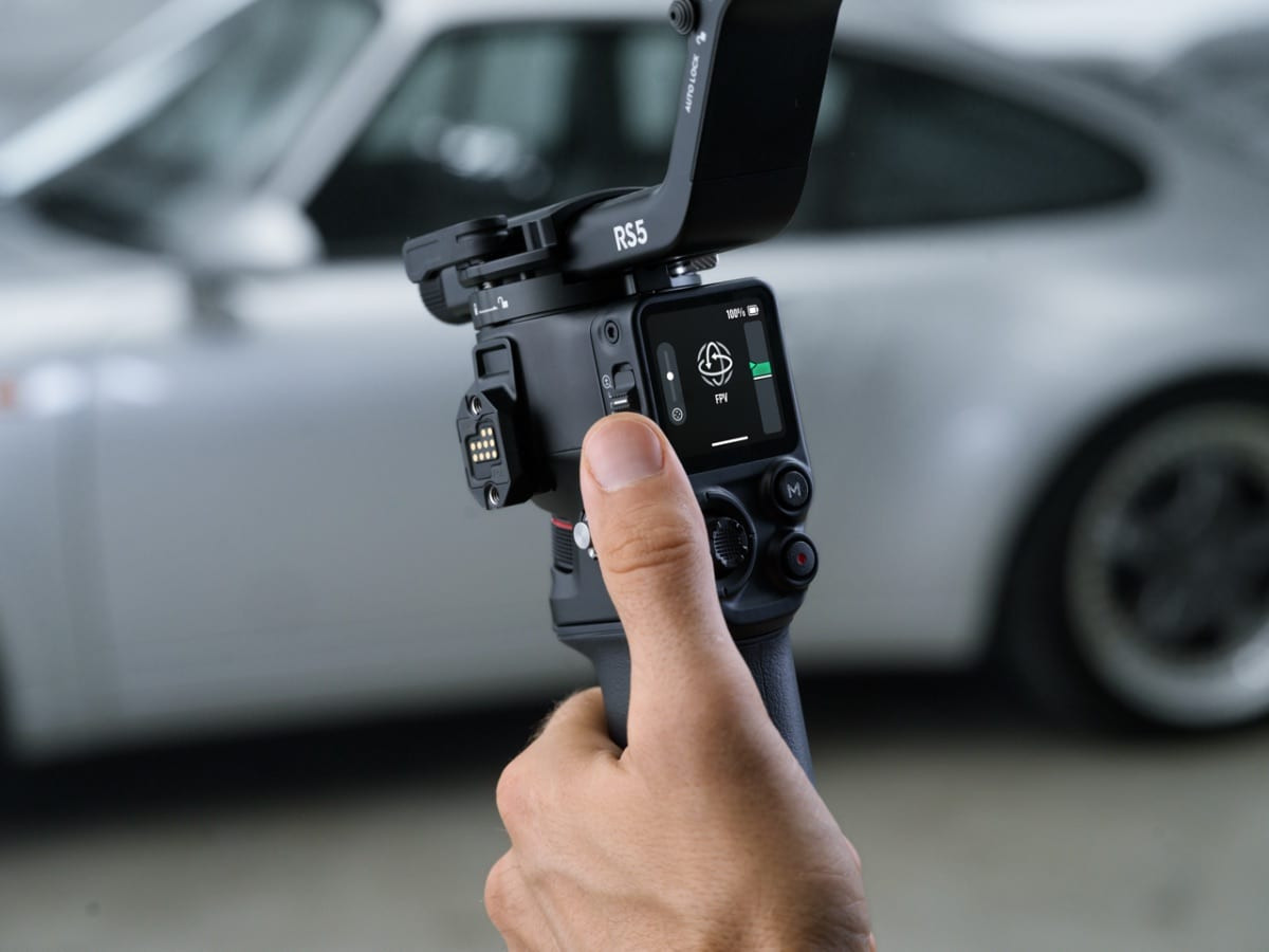 Ảnh chụp cận cảnh người dùng cầm gimbal RS 5 với màn hình hiển thị góc chụp trước xe hơi