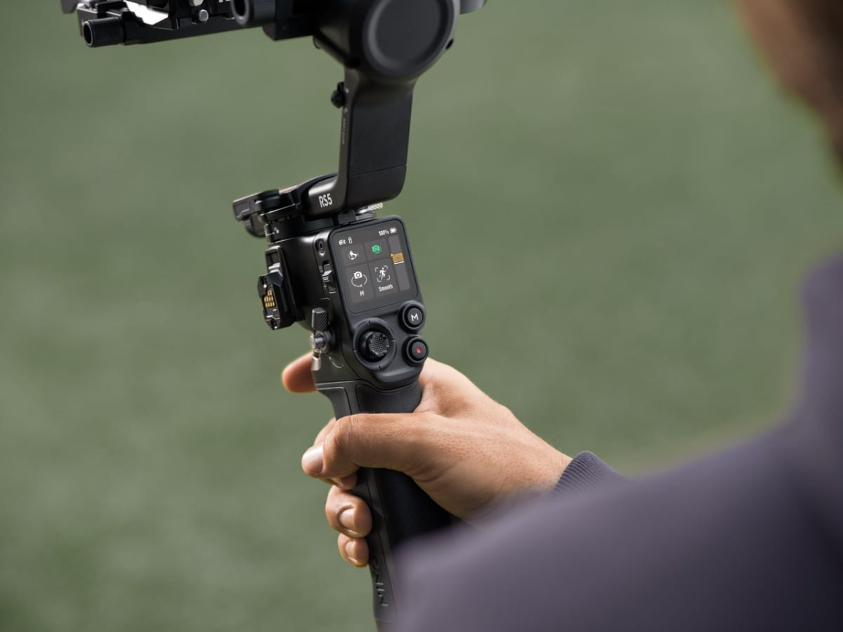 Cầm gimbal RS 5 màu đen chụp ảnh ngoài trời với phông nền sân cỏ xanh mờ ảo