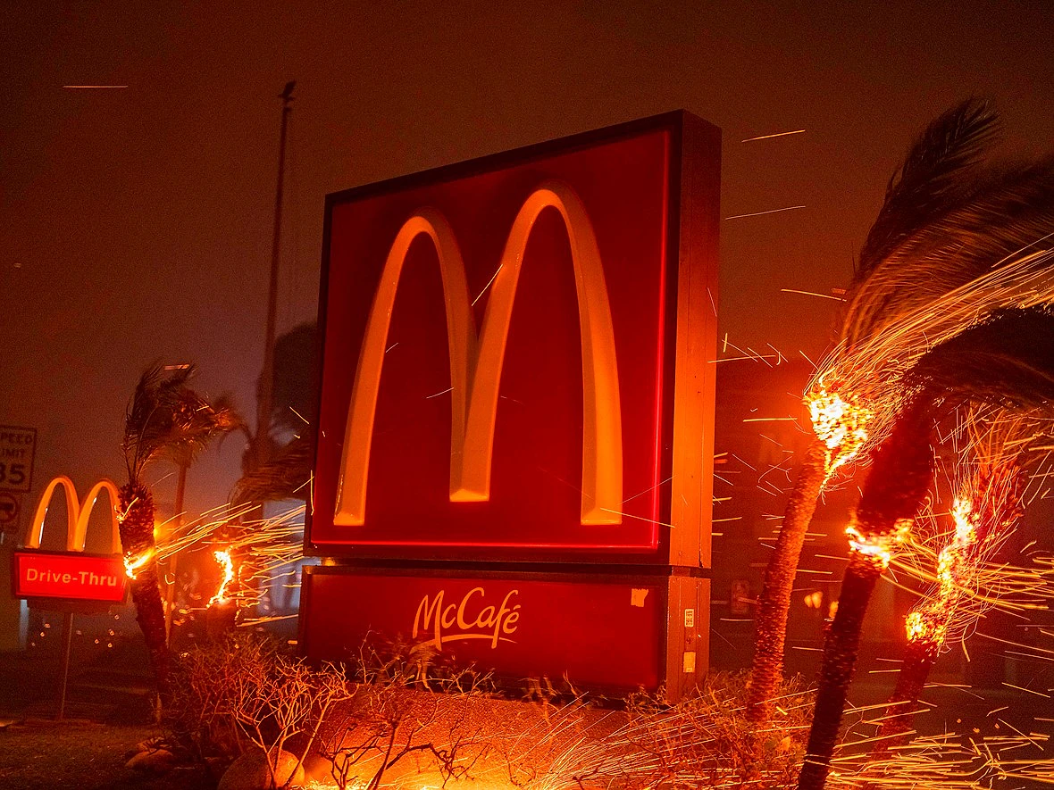 sparks fly from burning palm trees around a mcdonalds sign at night