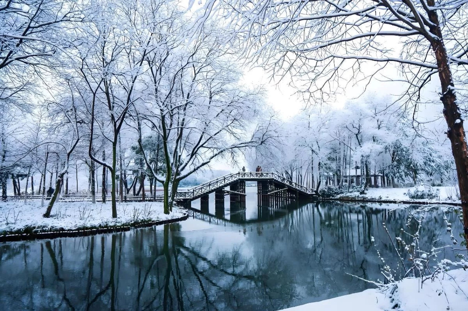 Snowy West Lake with willow trees and a wooden bridge over calm water