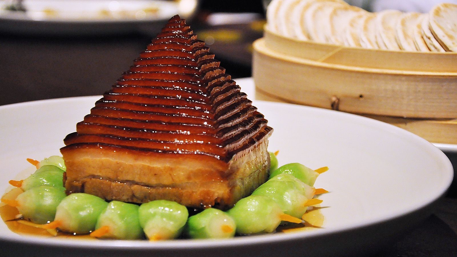 A classic pyramid stack of braised Dongpo pork belly with caramelized fat, served on a white plate with bok choy