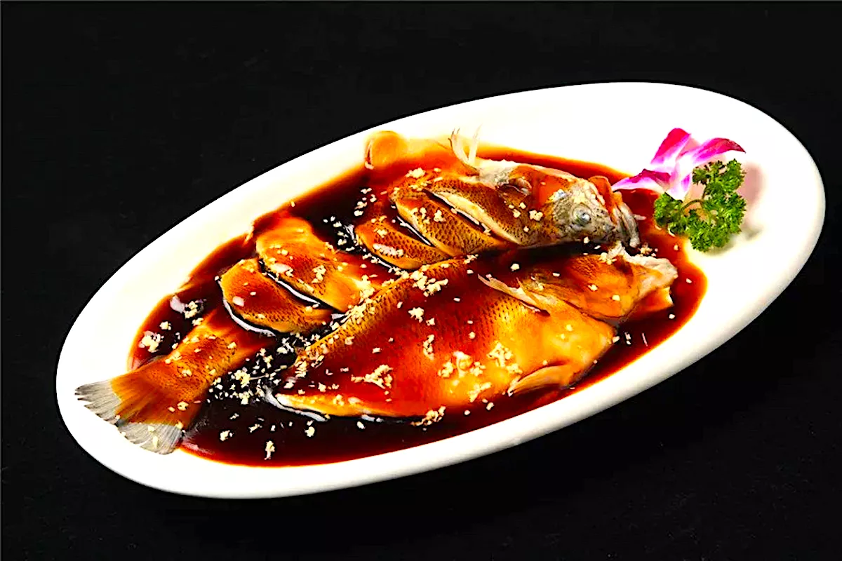 A whole grass carp poached and glazed with sweet vinegar and soy sauce, served on a white oval platter with a pink orchid garnish