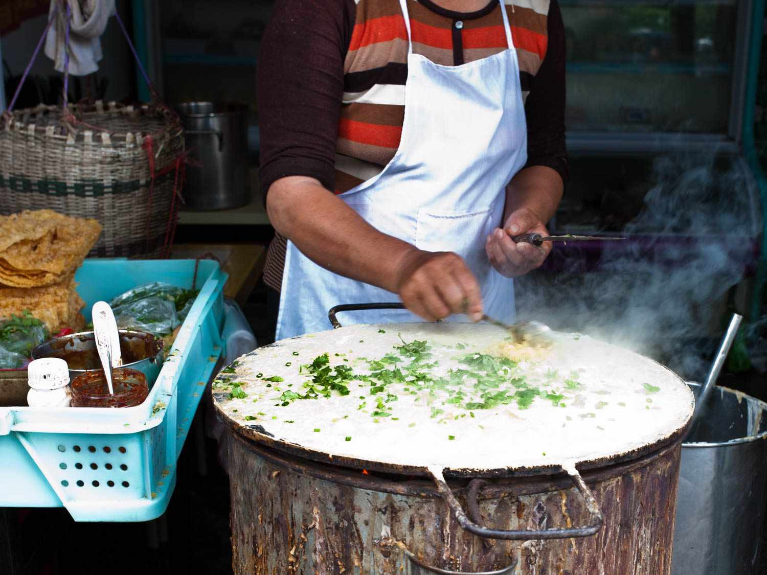 A woman vendor making a fresh jianbing on a circular griddle with cracked egg yolk spread across a green pancake