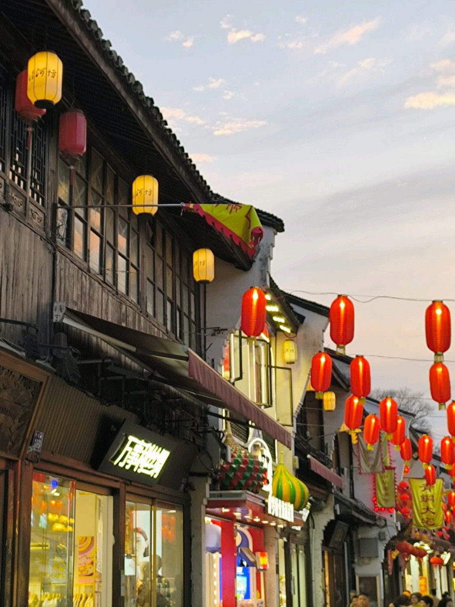 Hefang street lined with traditional wooden shopfronts, red and yellow lanterns hanging overhead at dusk