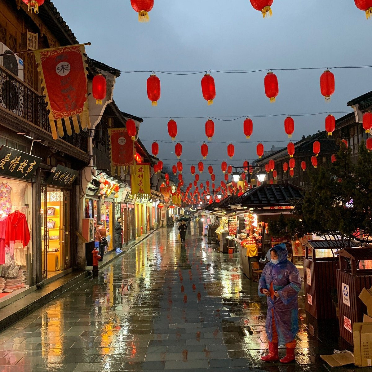 Hefang street with red lanterns stretching into the distance, traditional shopfronts, and a person in a raincoat on a wet stone street