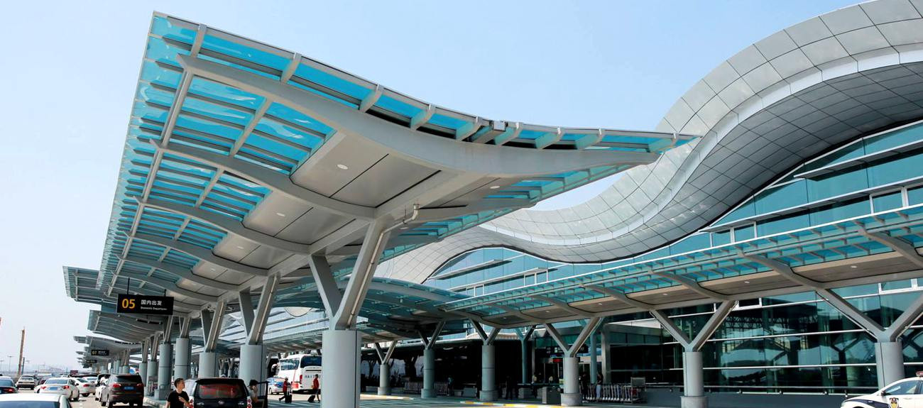 Hangzhou Xiaoshan airport departure drop-off area with modern glass canopy roof and cars at terminal entrance