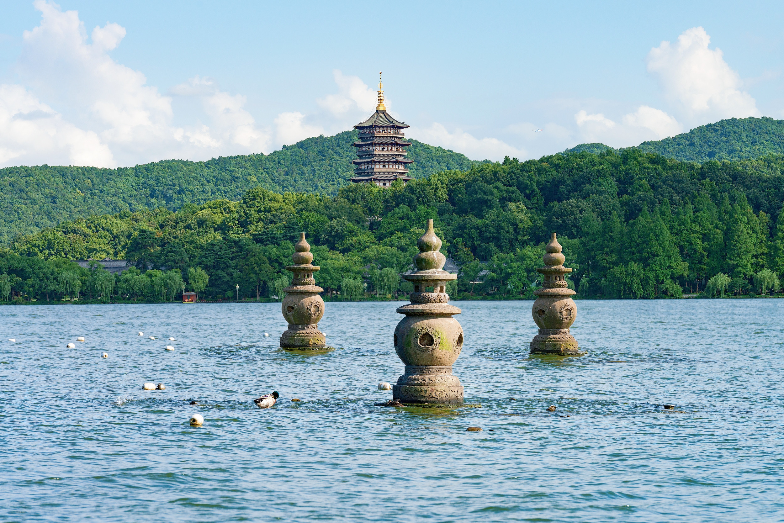 West Lake with three stone pagodas rising from the water in the foreground and Leifeng Pagoda on a forested hill in the background