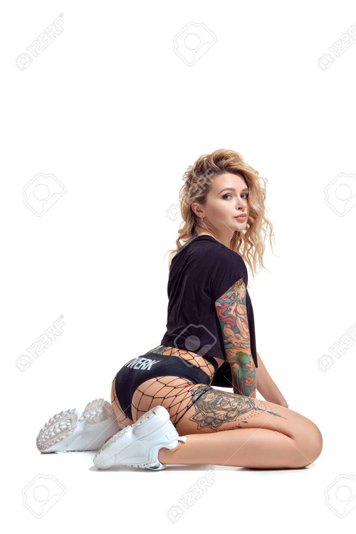 Wonderful blond twerk lady with tattoed body and long curly hair is posing sitting sideways on the f.jpg
