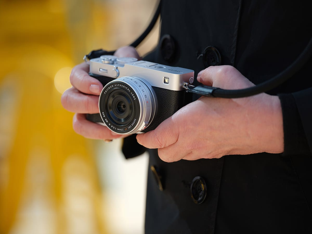 Người đàn ông cầm máy ảnh Fujifilm X-E5 và X-T30 III trước phông nền vàng tươi