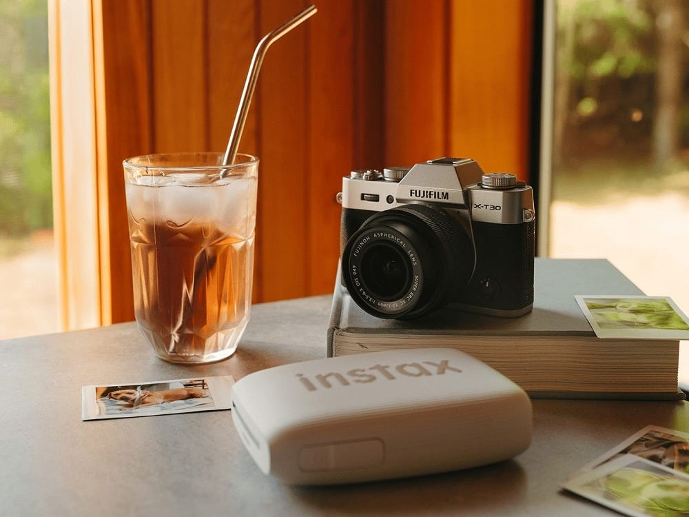 Bộ ảnh chụp trên bàn với máy ảnh Fujifilm X-T30 và máy in Instax cùng ly nước mát
